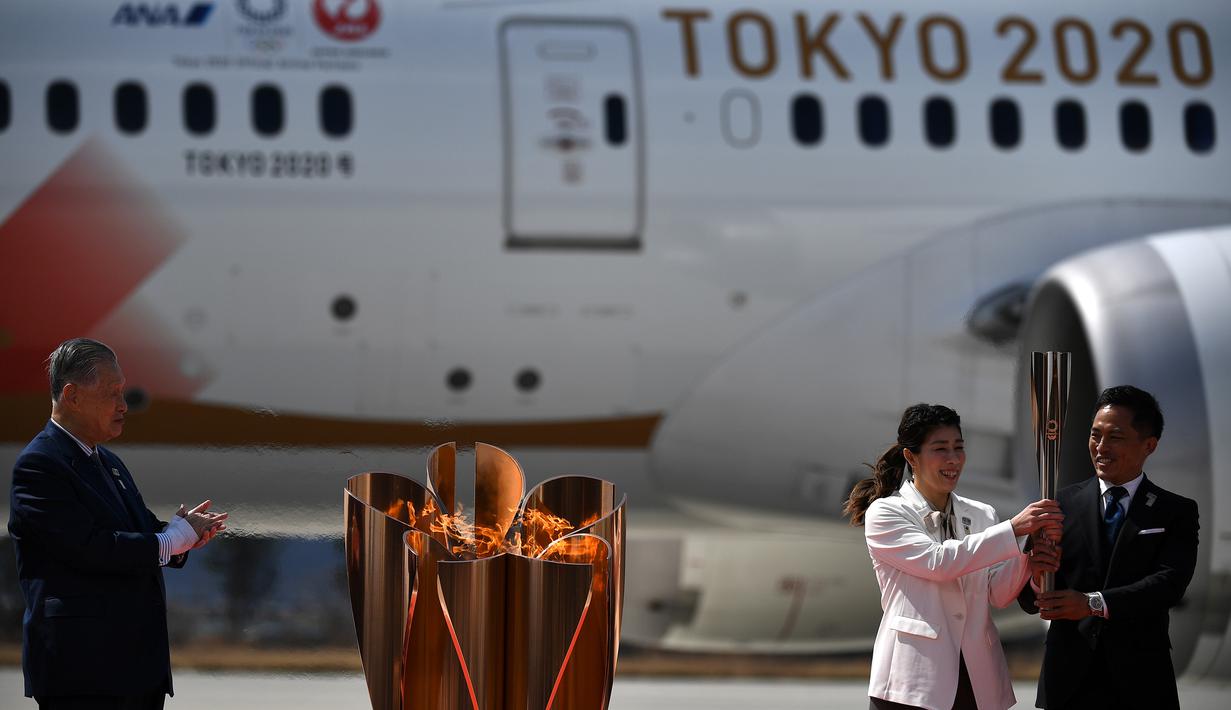 Presiden Olimpiade Tokyo 2020, Yoshiro Mori, menyaksikan dua atlet peraih tiga kali medali emas olimpiade Tadahiro Nomura dan Saori Yoshida menyalakan obor Olimpiade saat tiba dari Yunani di Pangkalan Udara Matsushima, Jepang, Jumat (20/3). (AFP/Philip Fong)