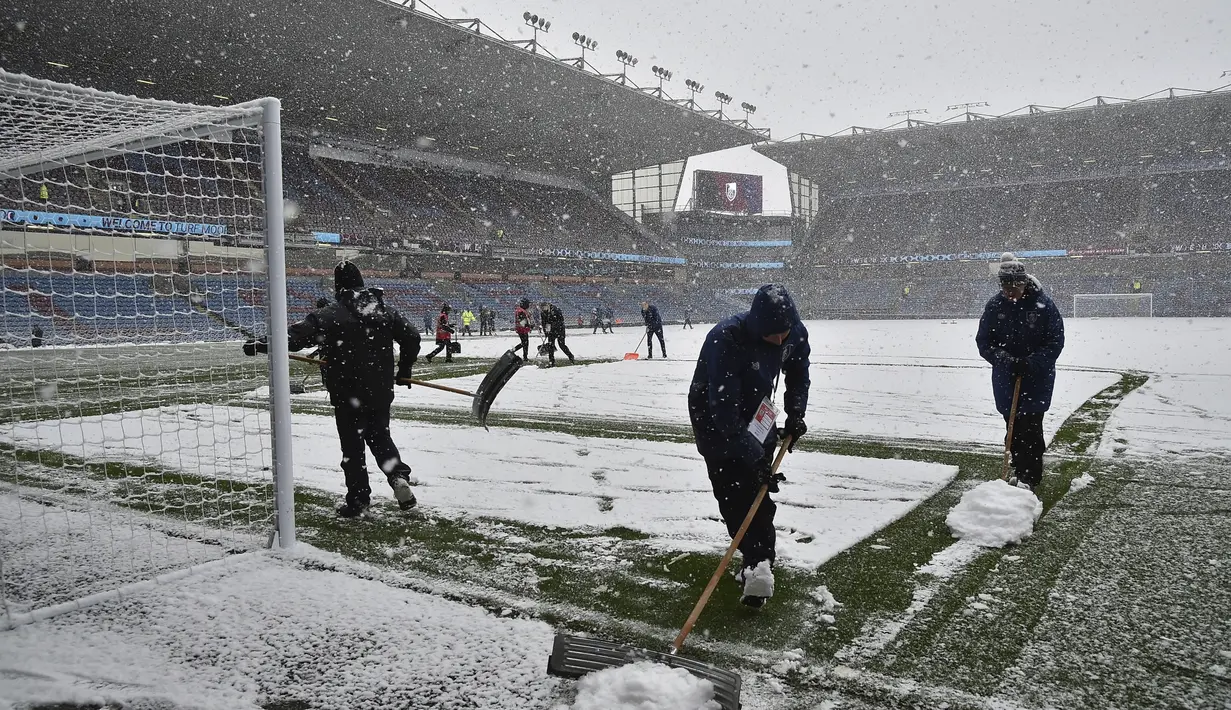 Pekerja staf membersihkan salju dari lapangan sebelum pertandingan antara Burnley dan Tottenham Hotspur di Turf Moor, Inggris, Minggu (28/11/2021). Baik pihak Burnley maupun Tottenham menerima keputusan ini. Mengenai tanggal pengganti, hal itu diputuskan di lain hari. . (AP Photo/Rui Vieira)