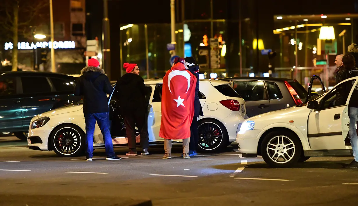 Warga Turki berkumpul membawa bendera negara Turki saat menggelar protes di Rotterdam, Belanda (11/3). Belanda melarang Menteri Luar Negeri Turki, Mevlut Cavusoglu untuk mendarat di Rotterdam, Belanda. (AFP/Emmanuel Dunand)
