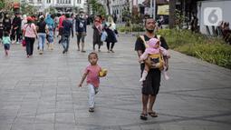 Seorang pria yang menggendong balita bejalan di kawasan wisata Kota Tua, Jakarta, Senin (23/1/2022). Kawasan wisata Kota Tua yang saat ini terbebas dari pedagang kaki lima (PKL) masih menjadi alternatif warga untuk mengisi liburan, termasuk cuti bersama menyambut perayaan Tahun Baru Imle 2023. (Liputan6.com/Faizal Fanani)