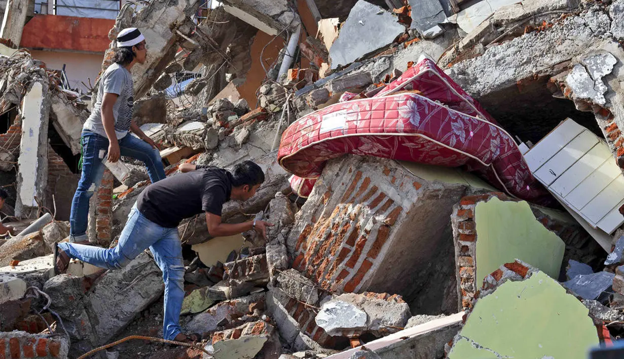 Warga memeriksa bangunan yang runtuh akibat gempa di Mamuju, Sulawesi Barat, Indonesia, Senin (18/1/2021). Hingga Minggu 17 Januari 2021 pukul 20.00 WIB, BNPB melaporkan jumlah korban meninggal akibat gempa Sulawesi Barat menjadi 81 orang. (AP Photo/Yusuf Wahil)