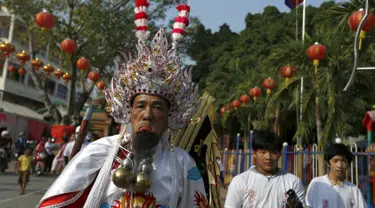 Seorang pria mengenakan kostum unik dengan kail tajam yang menembus pipinya dalam acara Hei Neak Ta atau parade roh untuk memperingati Cap Go Meh, Kamboja, (21/2). Cap Go Meh merupakan rangkaian acara dari tahun baru Imlek. (REUTERS/Samrang Pring) 	