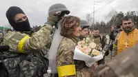 Seorang tentara memegang helm sebagai tiara mahkota pada upacara pernikahan anggota Pasukan Pertahanan Teritorial Ukraina Lesia Ivashchenko dan Valerii Fylymonov di pos pemeriksaan di Kiev, 6 Maret 2022. Kedunya menikah dengan upacara seadanya yang dilakukan korps mereka. (AP/Efrem Lukatsky)