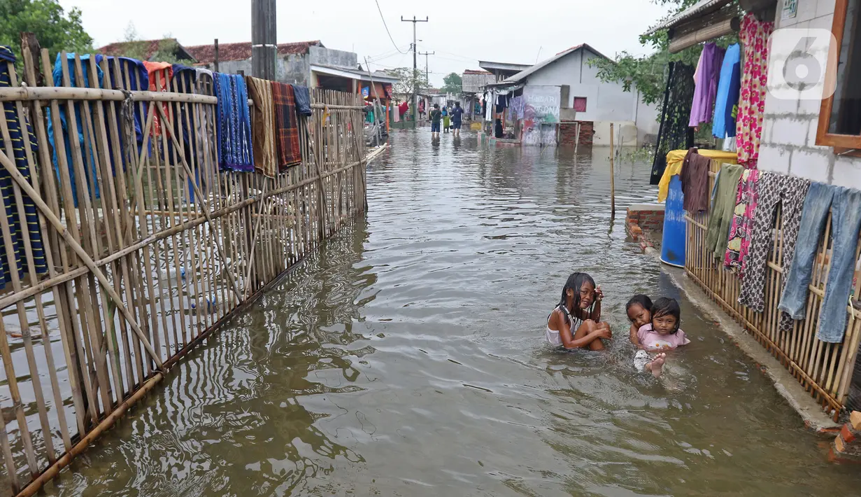 Anak-anak bermain banjir rob yang menggenangi rumah dan tambak warga di Desa Pantai Mekar, Muaragembong, Kabupaten Bekasi, Jawa Barat, Senin (6/12/2021). Banjir rob telah menggenangi wilayah tersebut selama empat hari akibat kenaikan permukaan air laut. (Liputan6.com/Herman Zakharia)