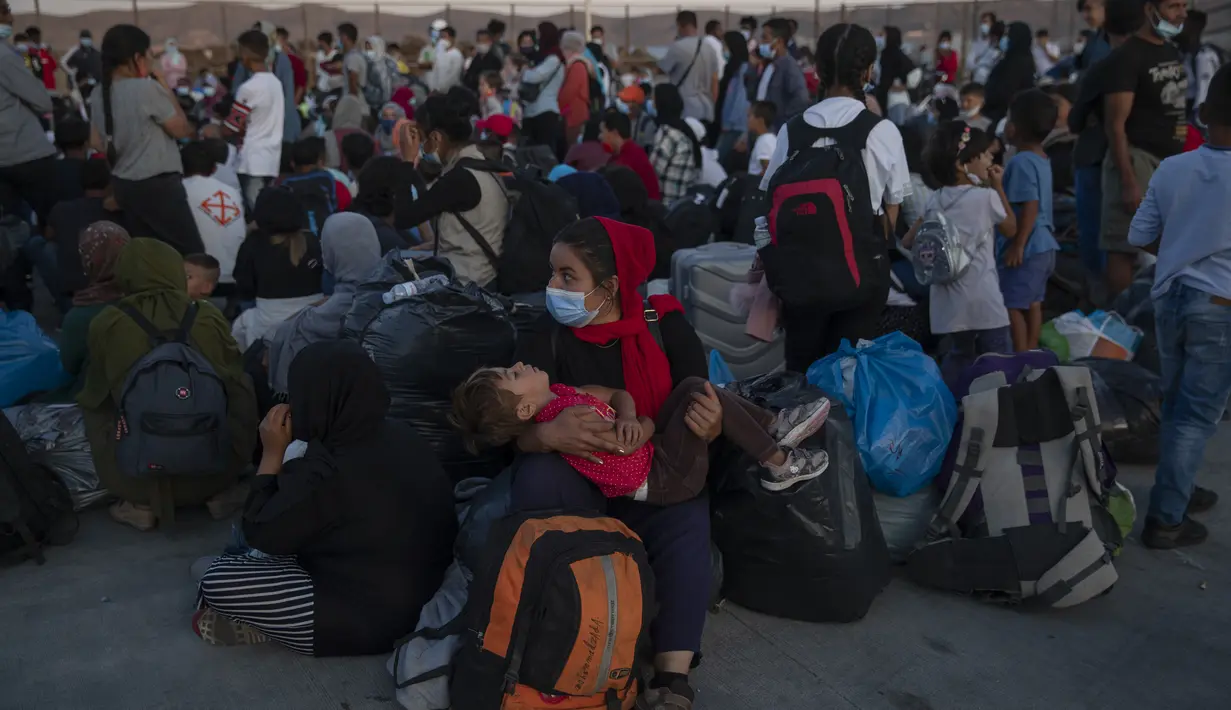 Pengungsi dan migran yang mengenakan masker pelindung untuk membantu mencegah penyebaran virus corona menunggu untuk naik bus setelah mereka tiba di pelabuhan Lavrio, sekitar 75 kilometer (48miles) selatan Athena (29/9/2020). (AP Photo/Petros Giannakouris)