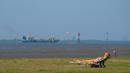 Seorang wanita berjemur ketika kapal kargo menuju Laut Utara saat suhu mencapai 34 derajat Celcius di dekat pantai Laut Utara di Wremen, Jerman barat (24/7/2019). (AFP Photo/Patrik Stollarz)