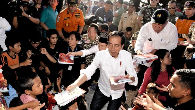 Presiden Joko Widodo atau Jokowi bersama Gubernur NTB Tuan Guru Bajang (TGB) Zainul Majdi membagikan buku saat mengunjungi korban gempa di lapangan Desa Madayin, Sambelia, Lombok Timur, NTB, Senin (30/7). (Agus Suparto/Indonesian Presidential Palace/AFP)