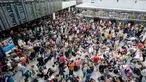 Calon penumpang berkumpul di depan papan jadwal penerbangan di Terminal 2 Bandara Munich, Sabtu (28/7). Kepolisian Jerman menutup terminal 2 bandara tersebut setelah seorang wanita dilaporkan menyusup melewati pos pemeriksaan. (MATTHIAS BALK /DPA/AFP)
