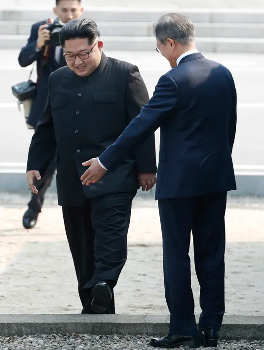Presiden Korea Selatan, Moon Jae-in mempersilahkan Pemimpin Korea Utara, Kim Jong-un melintasi perbatasan yang ditandai dengan tembok beton pendek setinggi mata kaki di Zona Demiliterisasi (DMZ), Panmunjom, Jumat (27/4).  (Korea Summit Press Pool via AP)