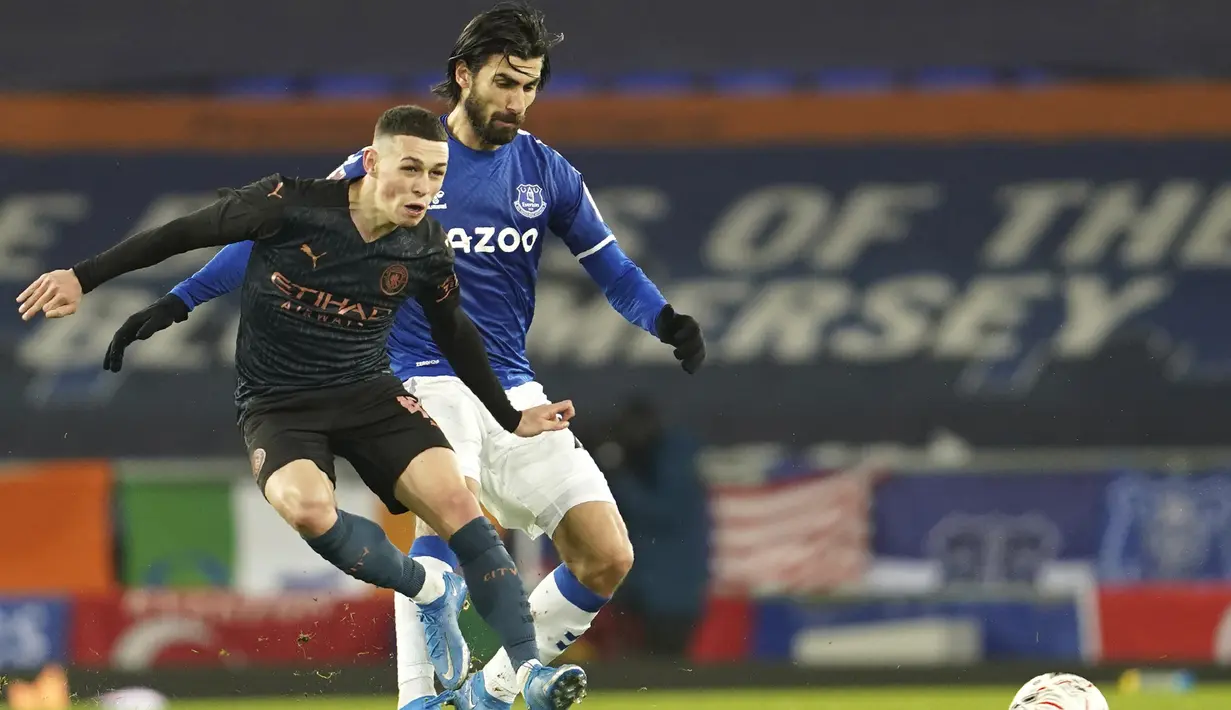 Gelandang Manchester City, Phil Foden (kiri) melepaskan tendangan di depan gelandang Everton, Andre Gomes dalam laga perempatfinal Piala FA 2020/2021 di Goodison Park, Liverpool, Sabtu (20/3/2021). Manchester City menang 2-0 atas Everton. (AP/Jon Super/Pool)