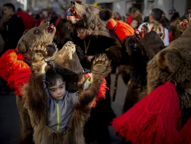 Anak-anak mengenakan kostum dari bulu beruang menari saat parade di Comanesti, utara Rumania, Jumat, 30 Desember 2022. Dentuman genderang dimulai pagi-pagi sekali menandakan kedatangan ratusan orang yang turun ke kota Comanesti yang mengenakan kostum terbuat dari bulu beruang dengan kepala yang masih menempel. . (AP Photo/Vadim Ghirda)