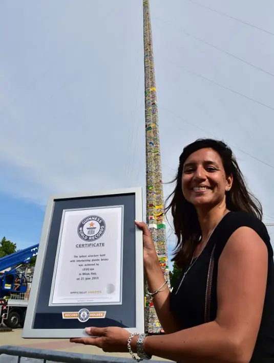 Seorang wanita berpose dengan sertifikat dari Guinness World Record, Itali, Minggu (21/6/2015).  Di belakang wanita tersebut tampak menara lego setinggi 35.50 meter. (AFP Photo/Giuseppe Cacace) 