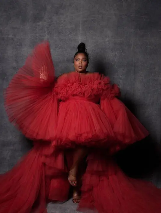 Lizzo tampil dramatis dalam balutan gaun tulle strapless crimson dengan lengan mengembang, rok tutu pendek yang dijepit di pinggang, dan long train.  Bintang pop itu menata gaun Giambattista Valli kustom itu dengan tumit sandal bertali merah yang serasi dan aksesori sederhana dengan anting-anting mutiara. (Instagram/lizzo).