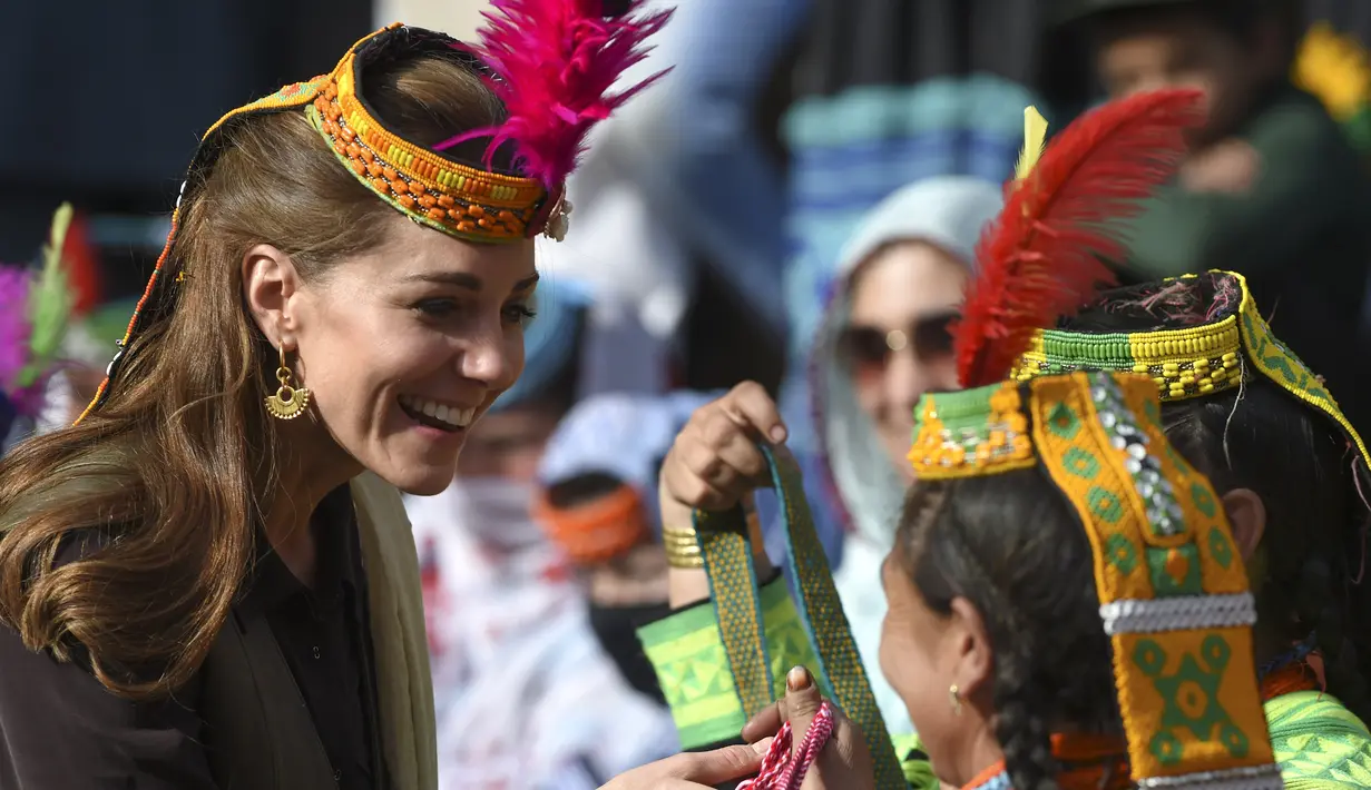 Duchess of Cambridge, Kate Middleton mengenakan topi tradisional suku Kalash tersenyum saat menerima hadiah dari seorang anggota suku Kalash selama kunjungannya ke Lembah Bumburate di Distrik Chitral utara Pakistan (16/10/2019). (AFP Photo/Farooq Naeem)