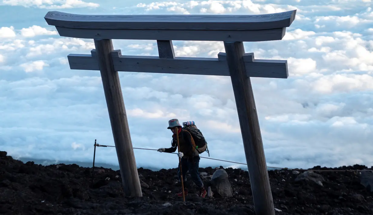 Seorang pria mencapai puncak Gunung Fuji, barat Tokyo pada 18 Juli 2021. Mendaki Gunung Fuji bukanlah hal yang mudah, tetapi pemandangan matahari terbit di atas lautan awan adalah hadiah terindah bagi yang mencapai puncak tertinggi di Jepang. (Charly TRIBALLEAU/AFP)