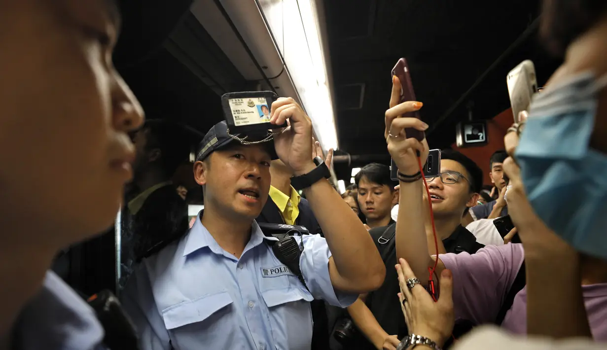 Seorang perwira polisi menunjukkan kartu anggotanya setelah pemrotes memintanya di sebuah stasiun kereta bawah tanah di Hong Kong (30/7/2019). Para Pengunjuk rasa telah mengganggu layanan kereta bawah tanah pada pagi hari. (AP Photo/Vincent Yu)