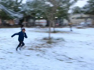 Seorang bocah berlari di atas salju yang turun di kota suci Karbala, Selasa (11/2/2020). Salju turun di Baghdad untuk pertama kalinya dalam satu dekade setelah sebelumnya ibu kota Irak itu sempat diguyur salju pada 2008, tetapi hanya berlangsung sekejap dan langsung mencair. (Mohammed SAWAF/AFP)