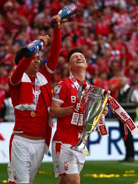 <p>Striker Nottingham Forest, Brennan Johnson (kiri) dan gelandang Joe Lolley merayakan dengan Trofi play-off Championship setelah kemenangan melawan Huddersfield Town di Stadion Wembley di London, Senin (30/5/2022). Nottingham Forest resmi kembali Premier League atau kasta tertinggi Liga Inggris usai absen selama 23 tahun. (AFP/Adrian Dennis)</p>