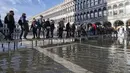 Orang menggunakan jembatan trestle untuk menyeberangi St Mark's Square yang dibanjiri air laut, di Venesia, Italia, Sabtu (4/12/2021). Air mencapai 99 sentimeter di atas permukaan laut dan bagian terendah kota tenggelam. (AP Photo/Luigi Costantini)