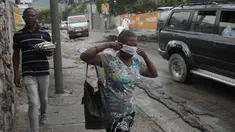 Seorang wanita berjalan melewati pihak berwenang setempat yang memindahkan jenazah pria yang dibakar massa di Port-au-Prince, Haiti, Selasa (25/4/2023). (AP Photo/Odelyn Joseph)
