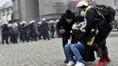 Dua orang membantu wanita yang terkena gas air mata saat demonstrasi menentang tindakan COVID-19 di Brussels, Belgia, Minggu (23/1/2022). Pengunjuk rasa juga mengkritik kebijakan wajib vaksin untuk beraktivitas di tempat umum maupun mengikuti kegiatan tertentu. (AP Photo/Geert Vanden Wijngaert)