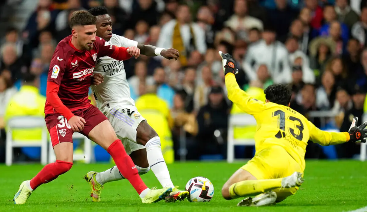 Pemain Real Madrid Vinicius Junior (tengah) berebut bola dengan kiper Sevilla Bono dan Jose Angel Carmona (kiri) pada pertandingan sepak bola Liga Spanyol di Stadion Santiago Bernabeu, Madrid, Spanyol, 22 Oktober 2022. Real Madrid menang 3-1 atas Sevilla. (AP Photo/Manu Fernandez)