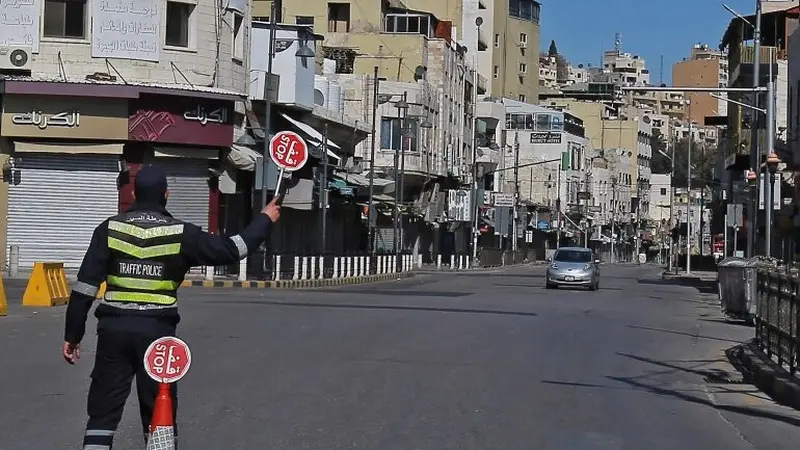 Seorang polisi memegang tanda berhenti di jalan yang hampir sepi di ibu kota Yordania, Amman, selama penguncian virus corona. [Khalil Mazraawi / AFP]