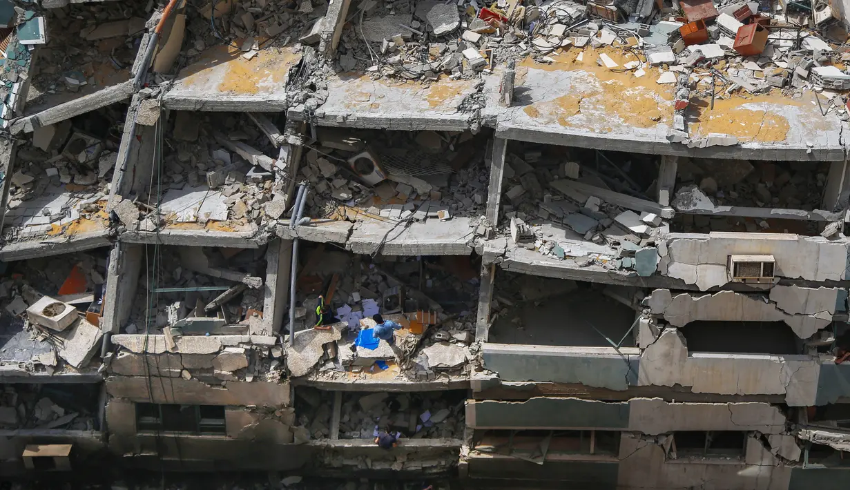 Warga Palestina memeriksa bangunan hancur yang menampung kantor The Associated Press dan media lainnya, setelah terkena serangan udara Israel pekan lalu, di Kota Gaza, Jumat (21/5/2021). Israel dan Hamas telah sepakat untuk gencatan senjata setelah 11 hari pertempuran. (AP Photo/Hatem Moussa)