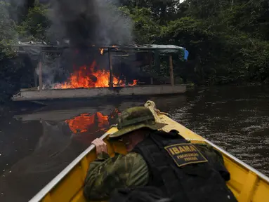 Petugas lingkungan Brasil saat berlindung dari kapal yang dibakar selama operasi terhadap penambangan emas ilegal di perairan hutan hujan Amazon, Roraima, Brasil (16/4). Daerah ini merupakan tempat dimana suku Yanomami tinggal. (REUTERS / Bruno Kelly)