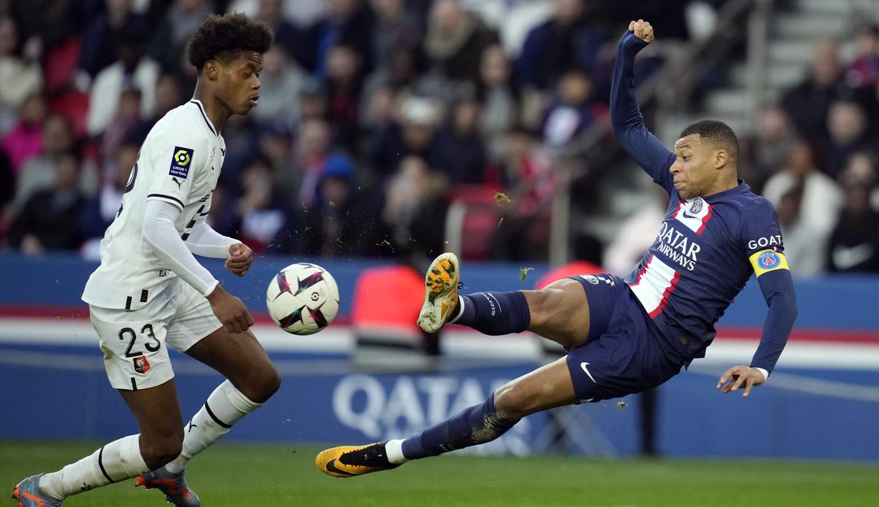 Penyerang Paris Saint-Germain (PSG) Kylian Mbappe menendang bola di sebelah bek Rennes, Warmed Omari pada  Ligue 1 2022/2023 pekan ke-28 di Parc des Princess, Senin (20/3/2023). (AP Photo/Christophe Ena)