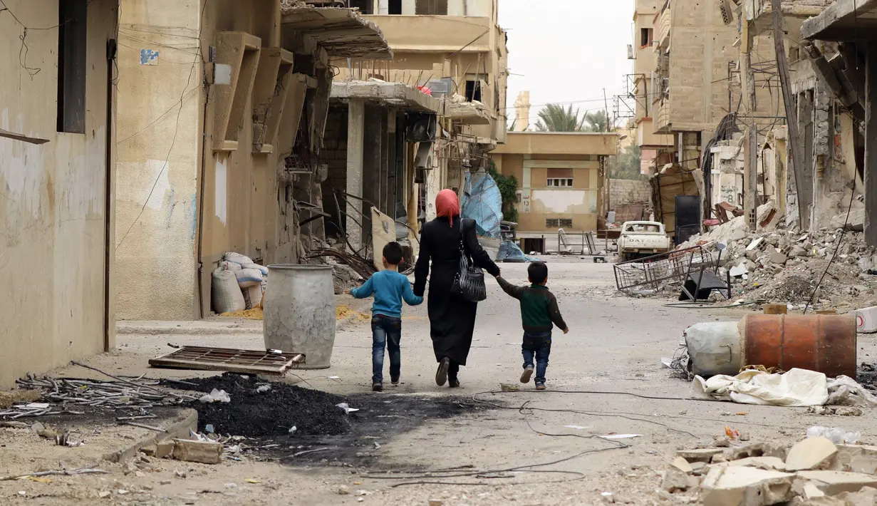 Seorang ibu bersama anaknya kembali ke rumah mereka di kota modern Palmyra, berdekatan dengan kota kuno Suriah, Sabtu (9/4). Kota itu berhasil direbut kembali oleh militer Suriah dari tangan kelompok ekstrimis ISIS beberapa waktu lalu. (Louai BESHARA/AFP)