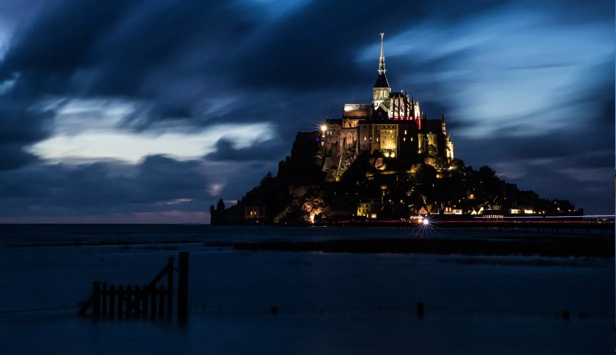 Kastil Mont Saint-Michel terlihat saat malam hari di Normandia, Prancis barat laut (31/8/2019). Mont Saint-Michel yang berjuluk ‘Wonder of the West’ bertengger di pulau berbatu di tengah gumuk pasir antara Normandia dan Brittany. (AFP Photo/Joel Saget)