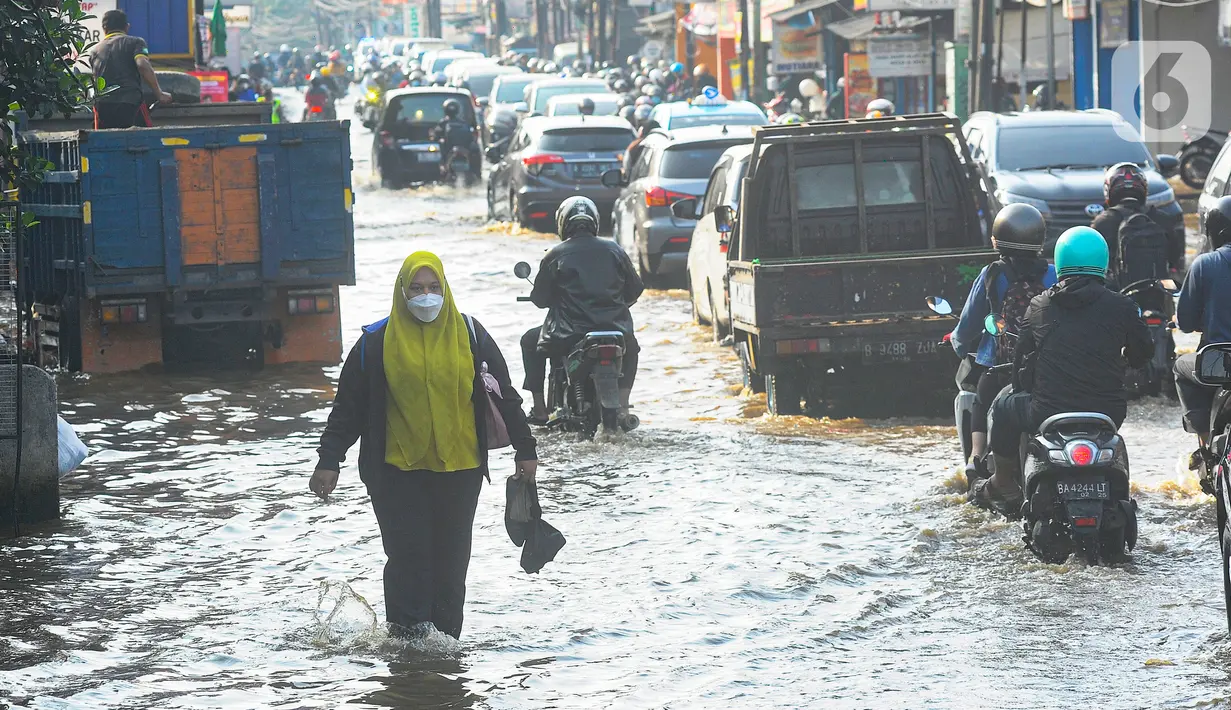 Warga berjalan melewati banjir yang menggenangi kawasan perempatan Mampang, Depok,Senin Rabu (19/6/2023). (merdeka.com/Arie Basuki)