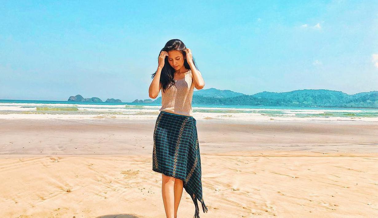 Penampilan dara kelahiran tahun 1997 ini sangat cerah saat berpose dengan latar belakang pantai pasir putih dan langit biru. Dengan baju berwarna putih dan Songket Bima berwarna gelap, tampak ia merapikan rambut hitamnya yang tergerai. (Liputan6.com/IG/indahpermatas)