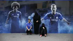Suporter Chelsea berfoto dengan latar poster pemain Chelsea di luat stadion Stamford Bridge. (AFP Photo/Adrian Dennis)