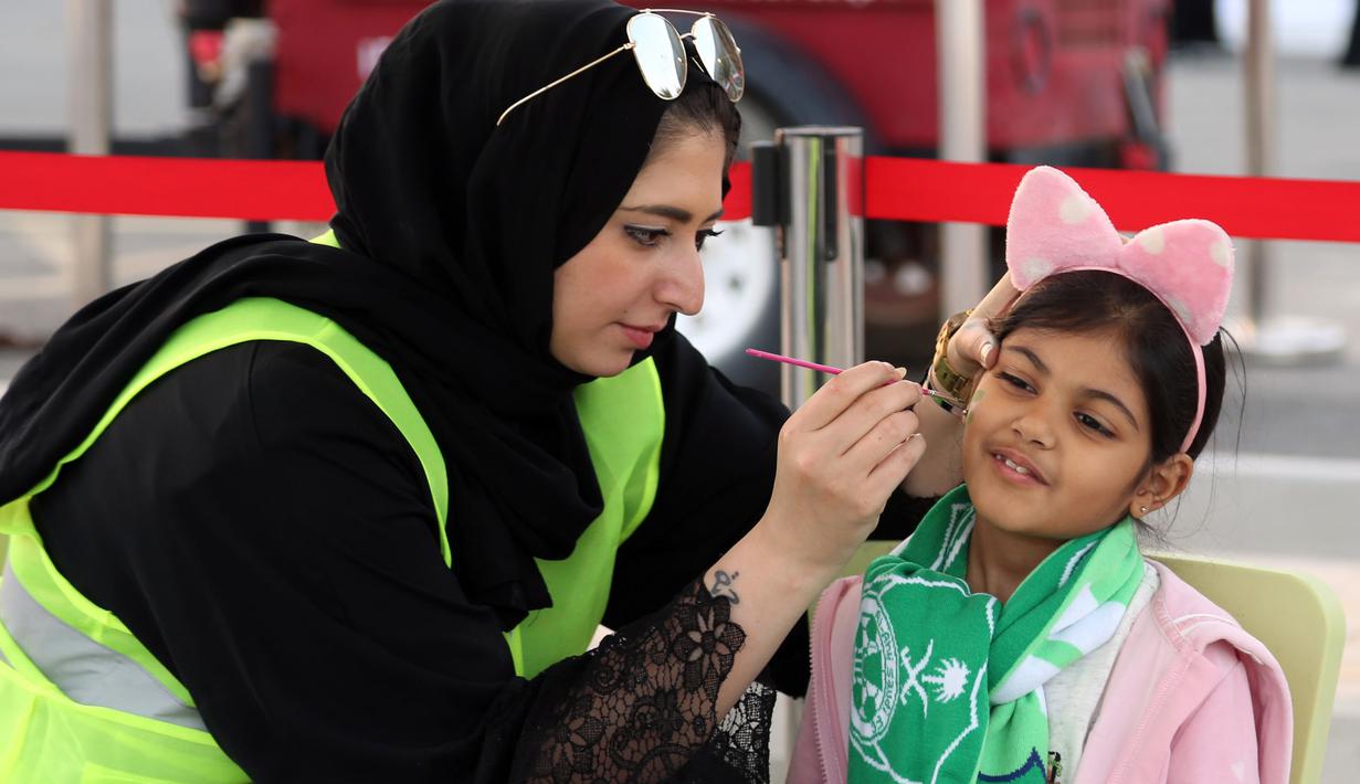 Supoerter wanita Al-Ahli menghias wajah anaknya sebelum menonton timnya melawan Al-Batin  pada laga Saudi Pro League di King Abdullah Sports City, Jeddah, (12/1/2018). Arab Saudi untuk pertama kalinya mengizinkan wanita menonton di stadion. (AFP/STRINGER)