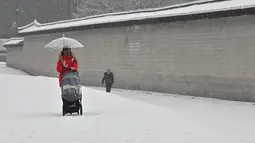 Seorang wanita mengendarai kursi dorong di sepanjang jalan yang tertutup salju di pusat kota Seoul (19/1/2022). Peringatan salju tebal telah dikeluarkan di seluruh kota pada pukul 9 pagi. (AFP/Jung Yeon-je)