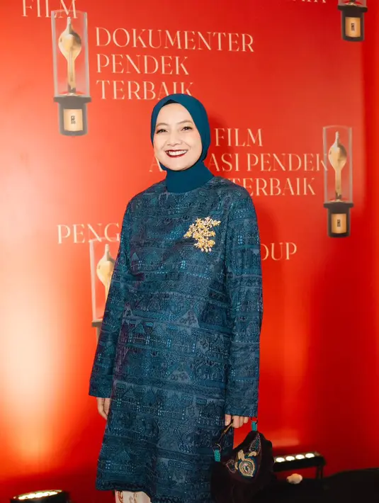 Cut Mini tampil santun dengan tunik tenun berwarna biru gelap dari Oscar Lawalata. Dipadukan dengan hijab berwarna senada dan kain batik sebagai rok [@snap.nuel]