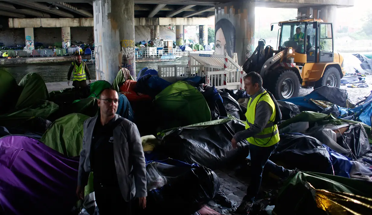 Pekerja balai kota Paris membersihkan sebuah tenda pengungsian migran di Paris, Prancis (30/5). Petugas mengerahkan buldoser untuk membersihkan tenda-tenda yang berada di bawah jembatan ini. (AP/Thibault Camus)