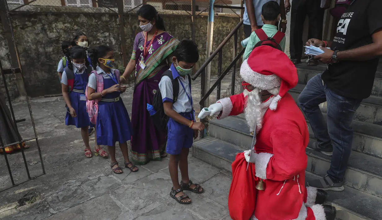 Seorang pria berkostum Sinterklas memeriksa suhu siswa setibanya mereka untuk memulai kelas di sebuah sekolah di Mumbai, India, Rabu (15/12/2021). Setelah ditutup selama hampir 20 bulan karena pandemi virus corona, sekolah di Mumbai dibuka kembali untuk kelas 1 sampai 7. (AP Photo/Rafiq Maqbool)