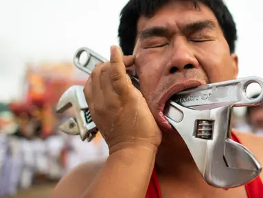 Penganut kuil Loem Hu Thai Su menusukkan kunci inggris ke pipinya saat festival vegetarian tahunan di Phuket, Thailand, Jumat (12/10). Acara ini dikenal juga dengan 'Nine Emperor Gods' atau hari 'Sembilan Kaisar Dewa'. (Jewel Samad/AFP)