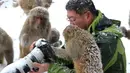 Seorang fotografer dikelilingi kera yang ingin melihat foto di kameranya saat salju turun di Wulongkou Nature Reserve, Tiongkok (6/1). Tingkah kera yang akrab dengan fotografer ini menjadi pemandangan menarik. (AFP Photo/China Out)