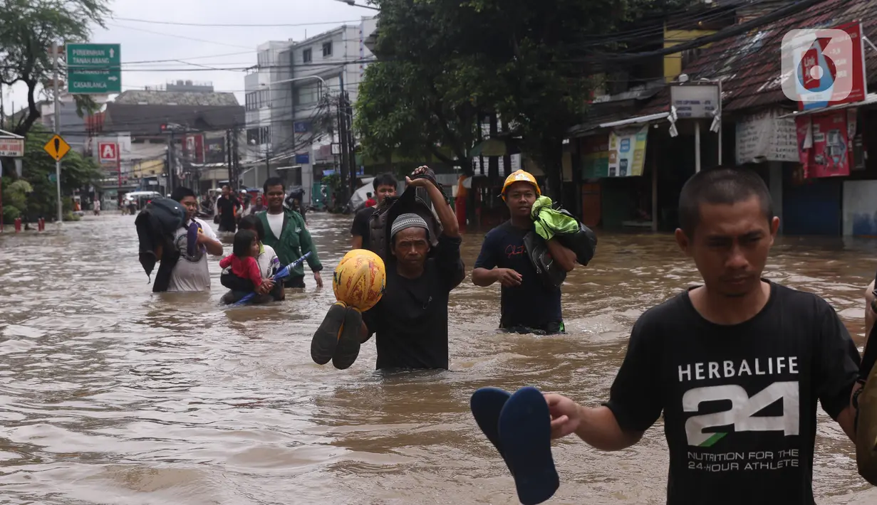 Warga melintasi banjir yang merendam Benhil, Jakarta, Selasa (25/2/2020). Hujan yang mengguyur wilayah tersebut membuat air sungai meluap sehingga menyebabkan Banjir setinggi pinggang orang dewasa. (Liputan6.com/Angga Yuniar)