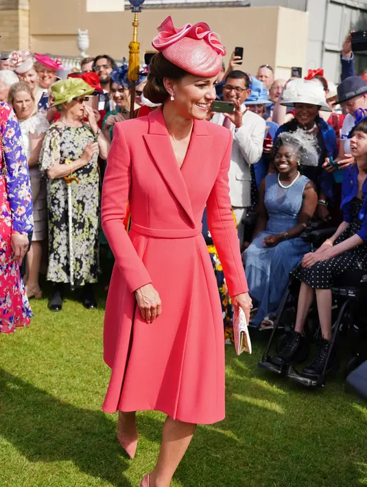 Kate Middleton, Duchess of Cambridge dari Inggris berbicara kepada para tamu di Pesta Taman Kerajaan di Istana Buckingham di London (18/5/2022). Kate Middleton memilih gaun mantel Emilia Wickstead versi koral yang telah ia kenakan pada beberapa kesempatan sebelumnya. (AFP/Pool/Dominic Lipinski)