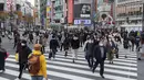 Orang-orang, yang mengenakan masker wajah, berjalan melintasi persimpangan di Tokyo (11/12/2020). Tokyo melaporkan 621 kasus COVID-19 baru pada hari Sabtu, 12 Desember, menetapkan level tertinggi baru di ibu kota Jepang. (AP Photo / Hiro Komae)