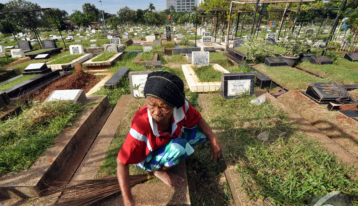Seorang pengurus makam membersihkan salah satu kuburan yang mulai ditumbuhi rumput liar di TPU Karet Bivak, Jakarta, Minggu (11/1/2015). (Liputan6.com/Miftahul Hayat)