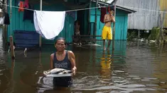 Edileuza Pereira da Silva membawa piring berisi ikan untuk dimasak di luar rumahnya, dibanjiri oleh naiknya sungai Negro di Iranduba, negara bagian Amazonas, Brasil, Senin (23/5/2022). Wilayah Amazon sedang dilanda banjir dengan 35 kotamadya yang menghadapi salah satu banjir terburuk mereka dalam beberapa tahun dan permukaan air diperkirakan akan meningkat selama beberapa bulan mendatang. (AP Photo/Edmar Barros)