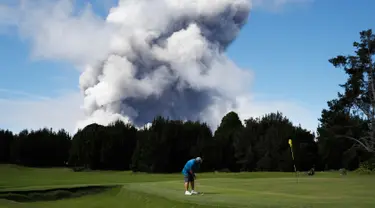 Doug Ralston bermain golf saat kepulan asap abu vulkanik berembus dari puncak gunung Kiluaea di Volcano, Hawaii (21/5). Lava dari gunung Kilauea Hawaii mengalir ke laut dan memicu reaksi kimia yang menciptakan asap hitam. (AP Photo/Jae C. Hong)
