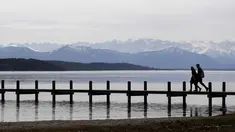 Pasangan berjalan di dermaga di depan pegunungan Alp di danau Starnberger See dekat desa Starnberg, Jerman selatan, selama cuaca musim semi dengan suhu 15 derajat pada 3 April 2018. (AFP Photo/Christof Stache)