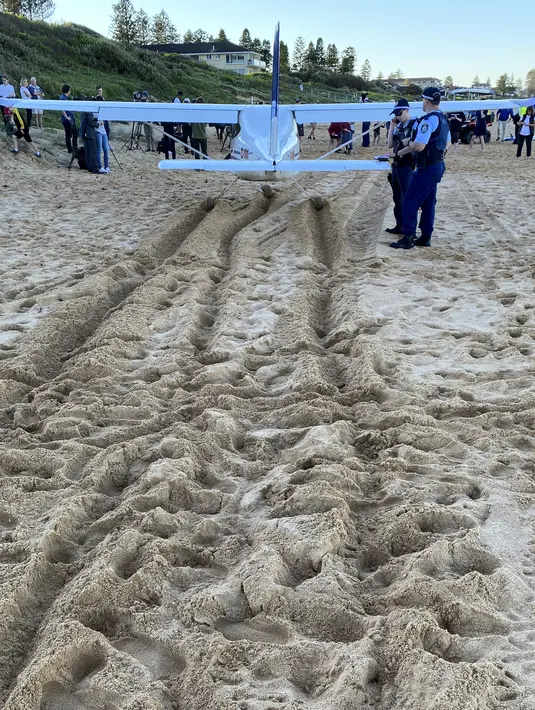 Polisi berdiri di dekat sebuah pesawat ringan yang melakukan pendaratan darurat di sebuah pantai di Sydney, Rabu (26/5/2021). Pesawat kategori rekreasi itu mendarat selamat di pantai Sydney dengan tiga orang di dalamnya termasuk seorang bayi setelah mengalami kerusakan mesin. (AP Photo/Mark Baker)